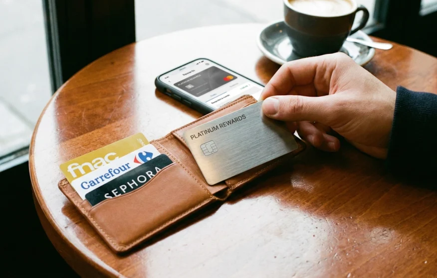Gros plan sur une carte bancaire Metal premium et des cartes de fidélité dans un portefeuille, posé sur une table de café pour illustrer le cumul du cashback.