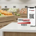 Photo en studio de la carte de fidélité physique Intermarché posée à côté d'un smartphone affichant le QR code de l'application mobile, dans un décor de rayon fruits et légumes.