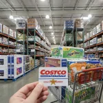 Carte de membre Costco tenue en main dans un entrepôt rempli de produits en gros.