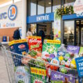 Caddie rempli de produits en gros volumes devant un magasin E.Leclerc avec des décorations printanières.
