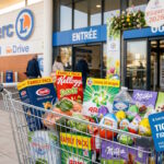 Caddie rempli de produits en gros volumes devant un magasin E.Leclerc avec des décorations printanières.