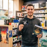 Joueur souriant utilisant sa carte de fidélité Mégacarte dans une boutique de jeux vidéo.
