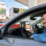 utomobiliste comparant ses applications et cartes de fidélité carburant sur son smartphone en station-service.