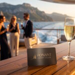 Carte de membre engravée du Ponant Yacht Club et coupe de champagne sur un pont en teck d'un yacht Ponant au coucher du soleil.
